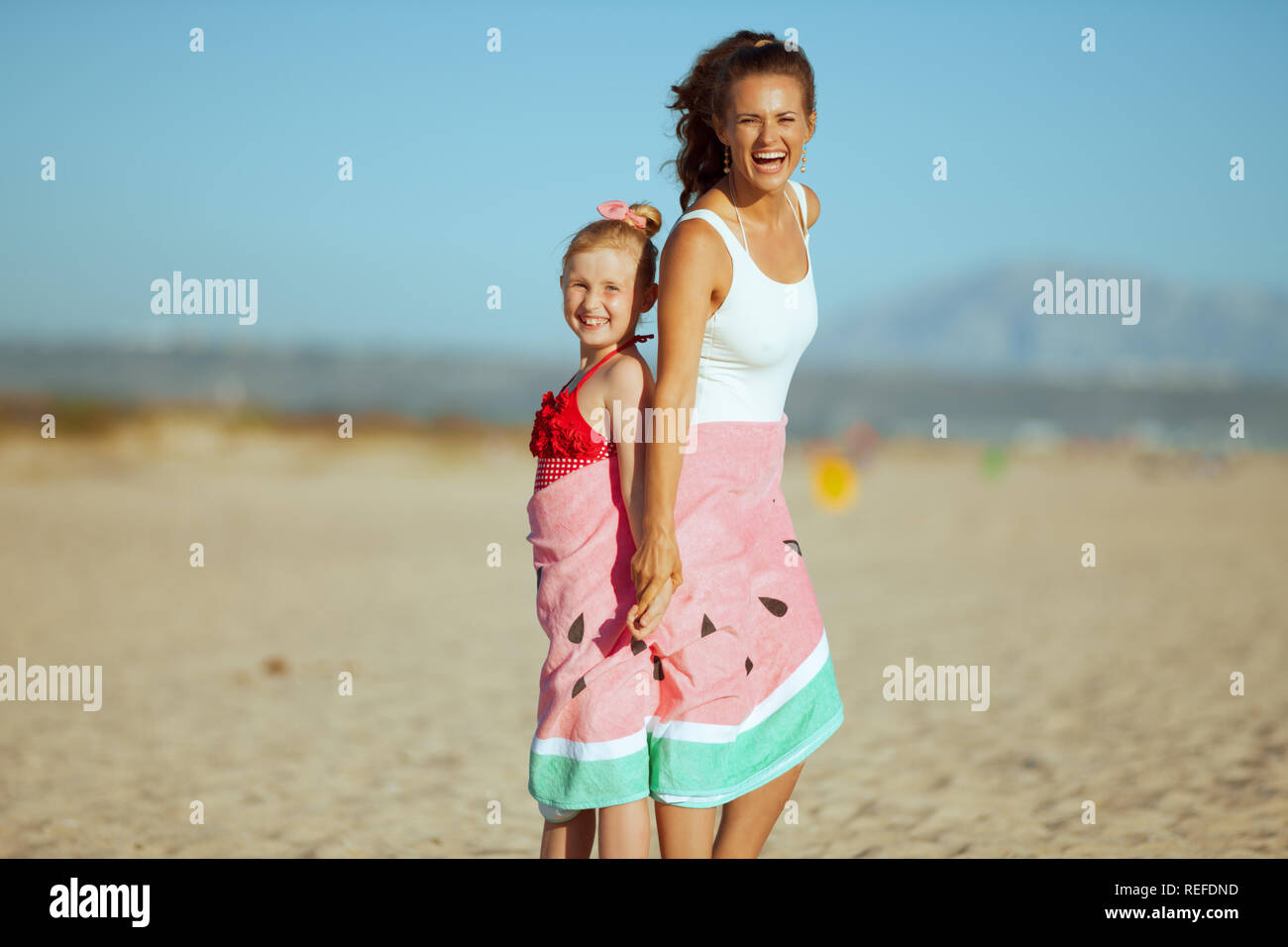Feliz joven madre e hija en traje de baño en la costa del océano por la  noche envuelta en una toalla de sandía. Playa - perfecto para mantenerse  activa y o Fotografía