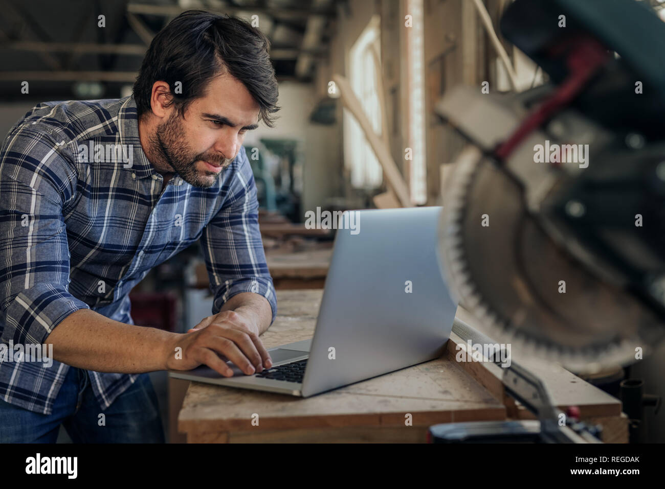 Carpintero trabajando en un portátil en su carpintería studio Foto de stock