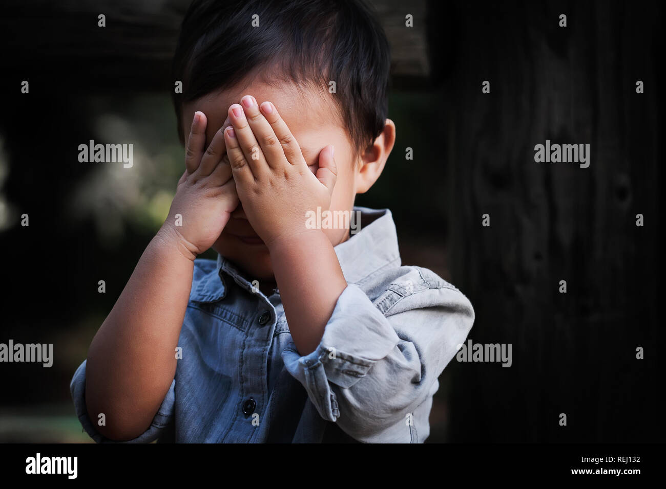 Un joven niño de edad que cubre su rostro con las manos, mostrando signos de ansiedad, miedo y decepción. Foto de stock