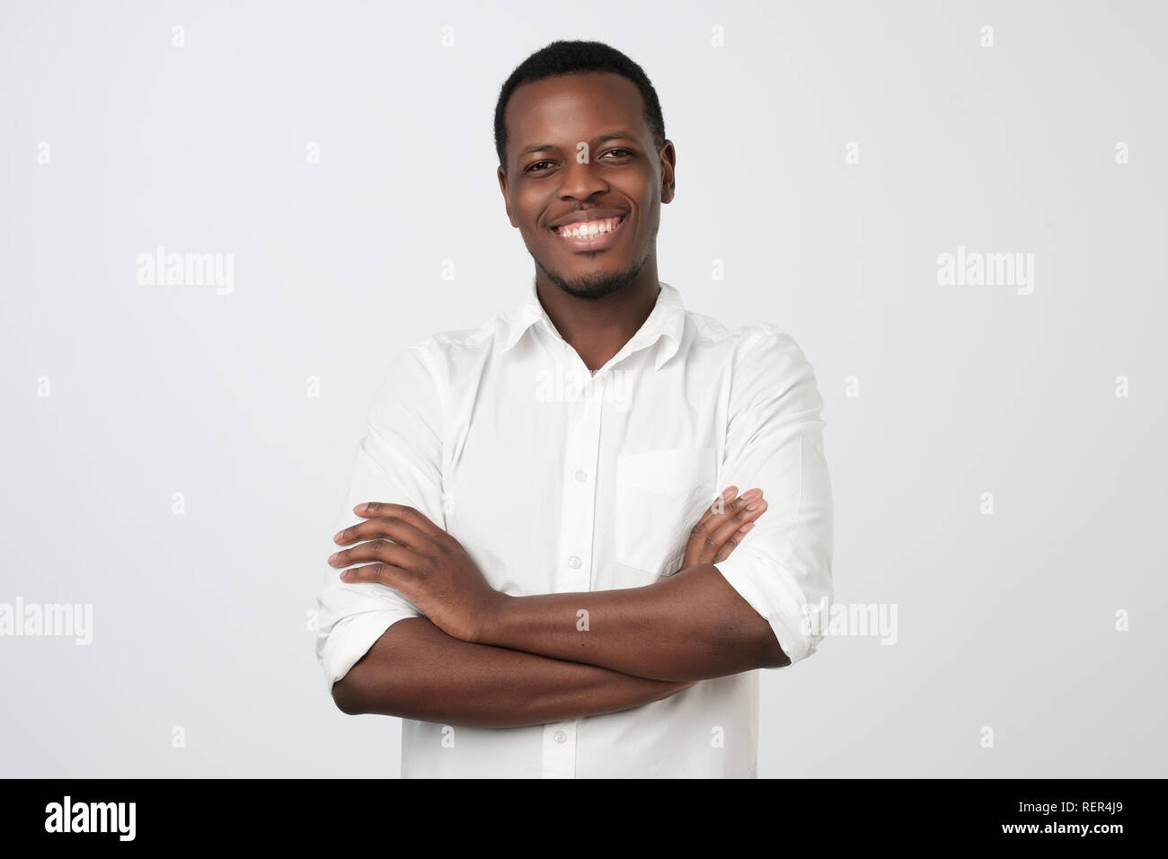 Retrato de éxito serio guapo afroamericanas hombre camiseta en manos cruzadas y sonriente Foto de stock