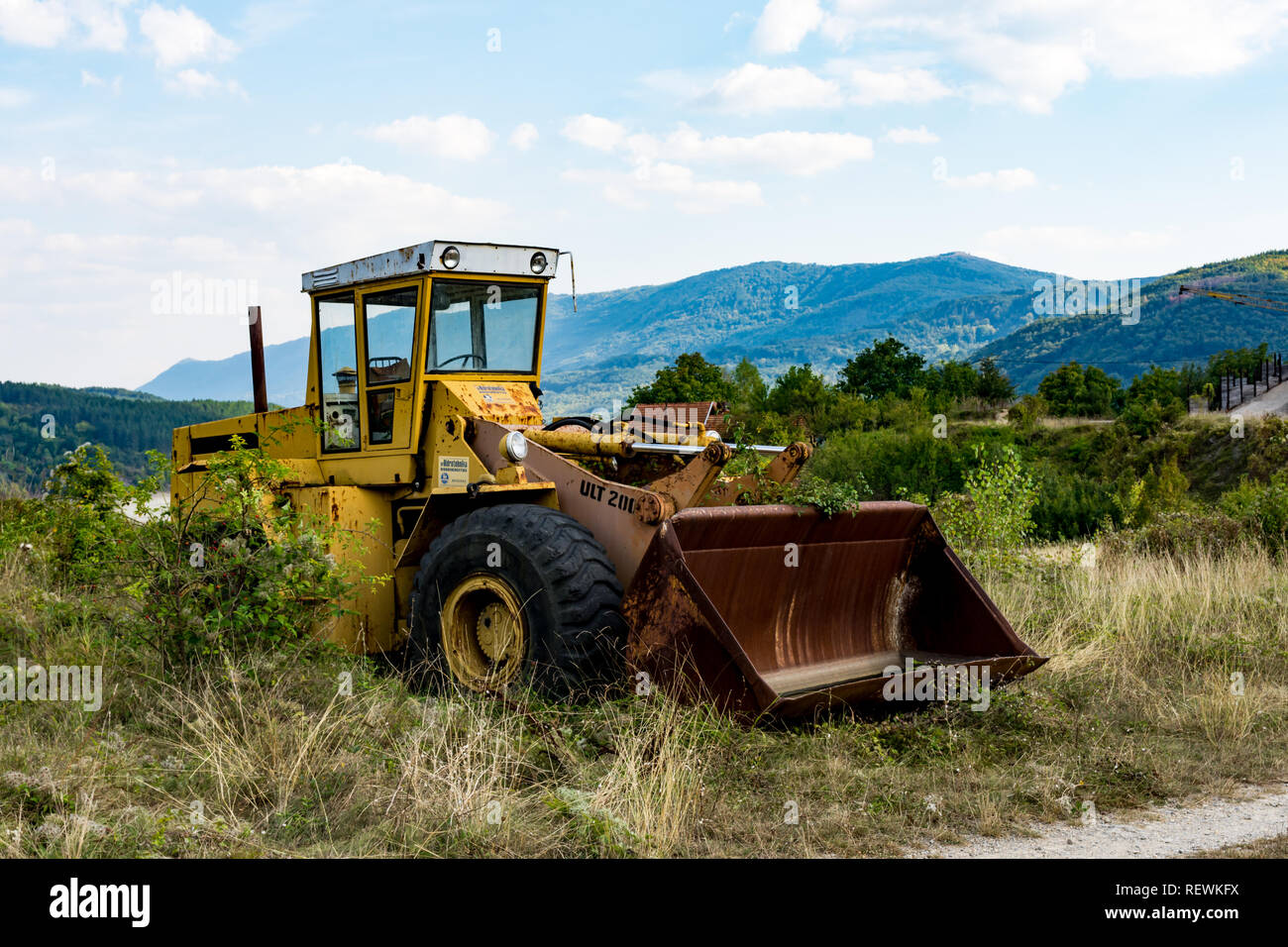 Viejos abandonados excavadora amarilla rota, cerca del lago Zavoj, sobre una montaña vieja. Oxidado y con los neumáticos dañados resistieron los dientes del tiempo. Foto de stock