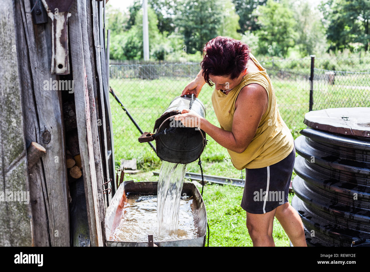 Una madre trabajadora llenando la cuenca superficial fuera del granero. La  mujer a acarrear agua desde el pozo natural. Quehacer doméstico típico.  Rurales Fotografía de stock - Alamy