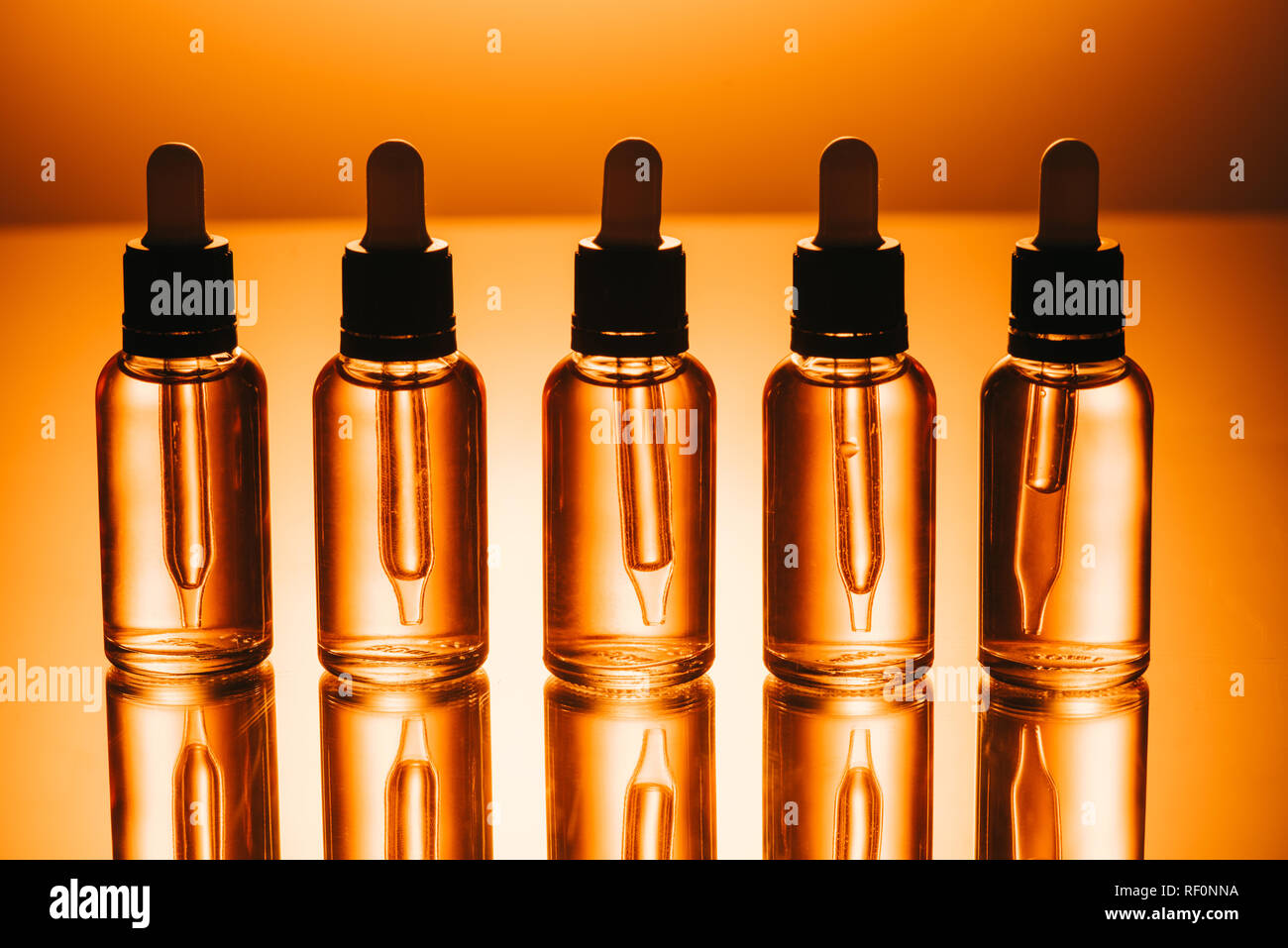 Fila de cbd aceite en botellas con cuentagotas sobre fondo naranja Foto de stock