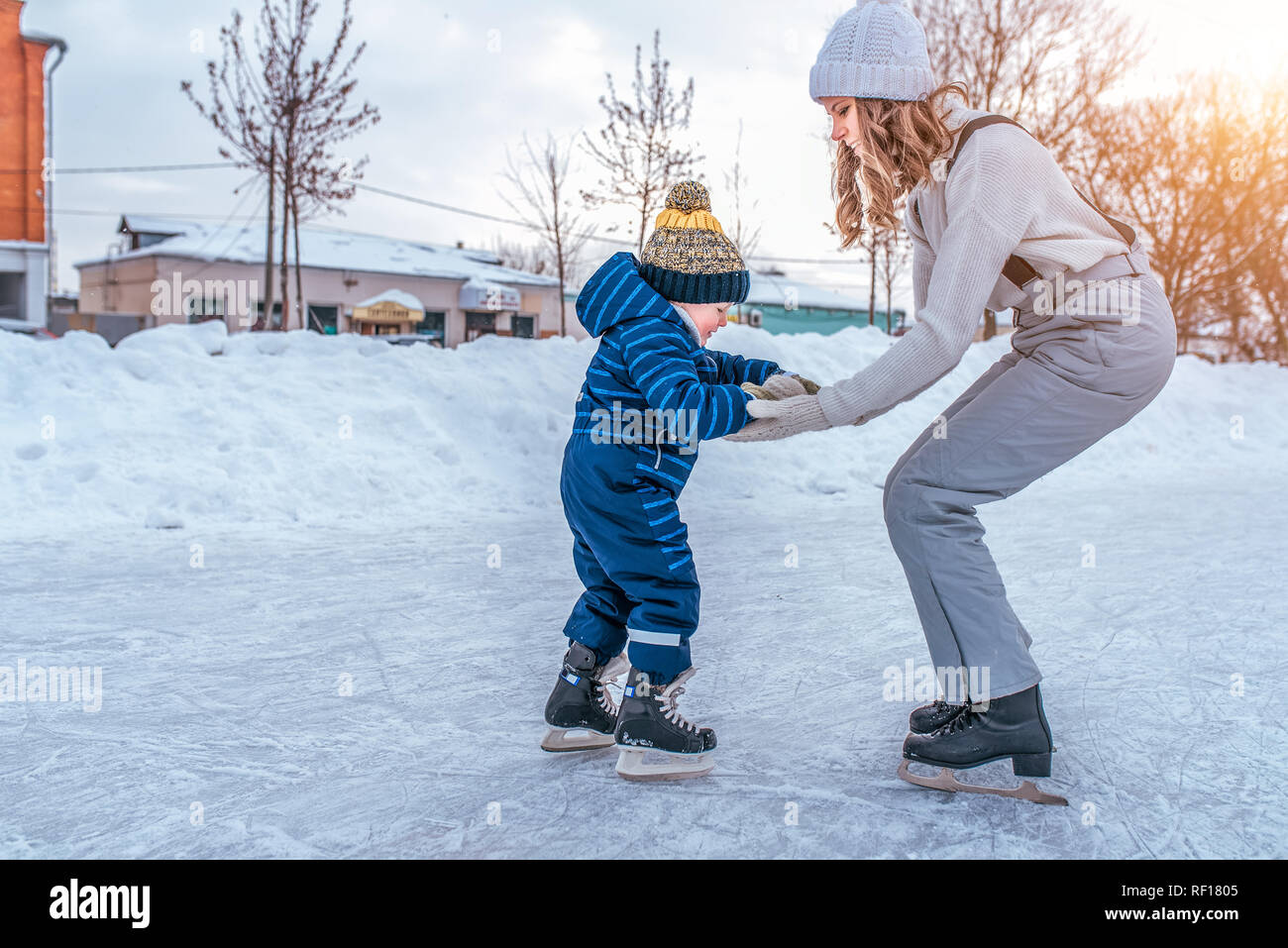 Un niño de 3-5 años de edad está patinando. Mamá mantiene a su hijo ayuda a  resistir. Primeros pasos sobre patines. En el invierno en la ciudad en la pista  de patinaje.