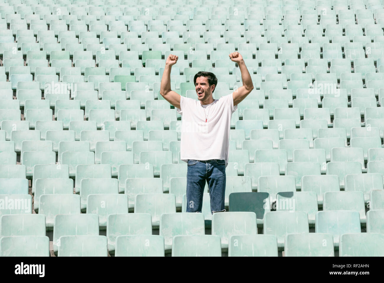 Un joven apuesto hombre permanece en un estadio vacío solos y celebra un triunfo y muestra una sensación de éxito Foto de stock