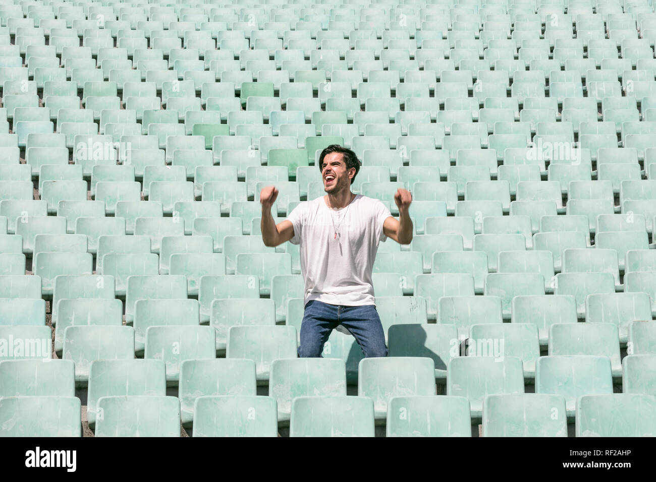 Un joven apuesto hombre permanece en un estadio vacío solos y celebra un triunfo y muestra una sensación de éxito Foto de stock