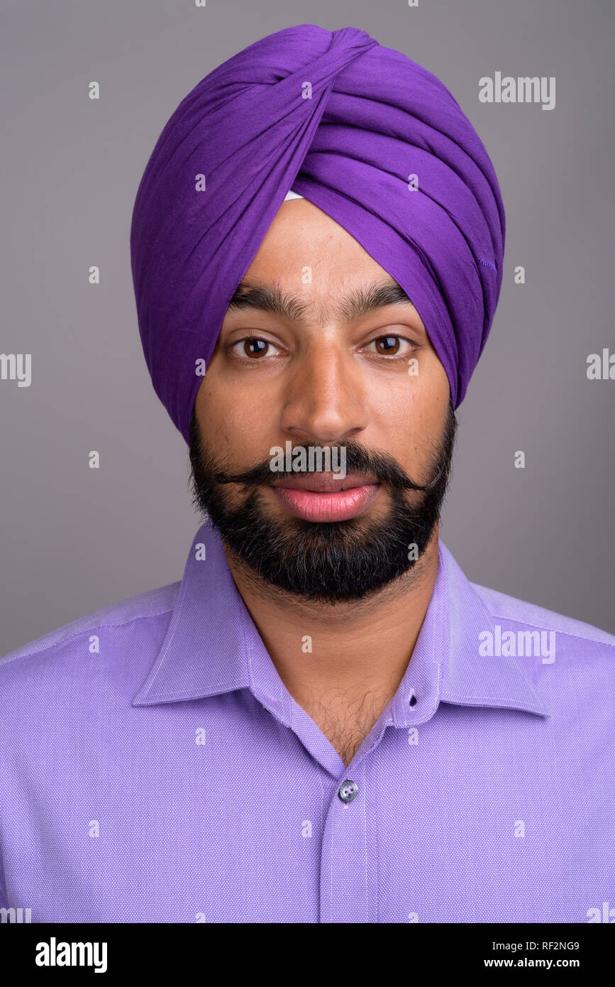 Joven hombre de negocios Sikh India guapo usando turbante contra fondo gris  Fotografía de stock - Alamy