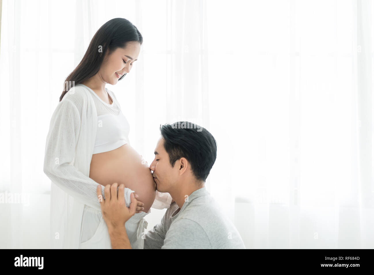 Esposo de Asia besar embarazada vientre de su esposa con los ojos cerrados. Matrimonio asiático y concepto de familia. Foto de stock