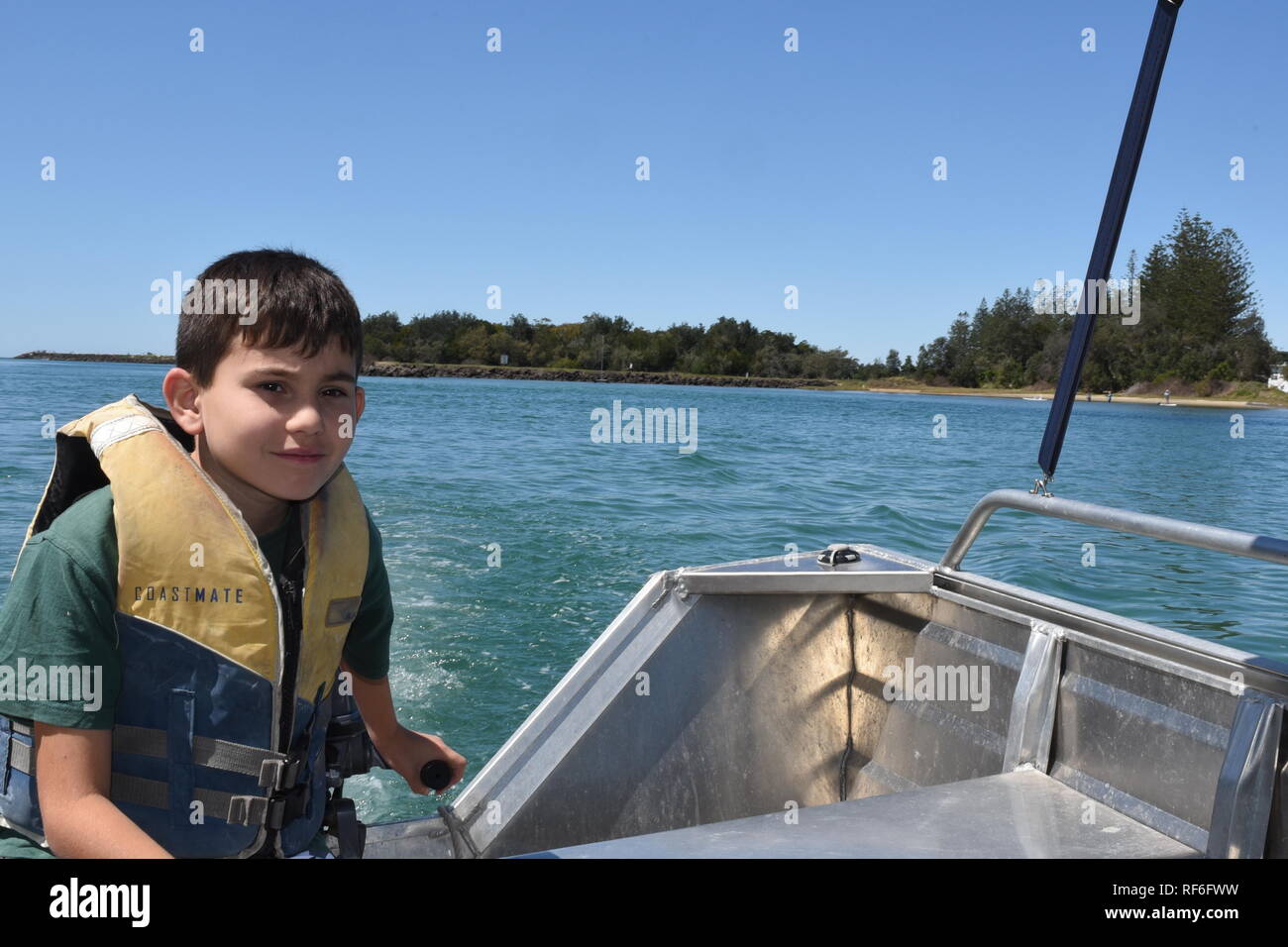 Un muchacho joven con un chaleco salvavidas, conduciendo un pequeño pequeño barco sobre el río de Brunswick, New South Wales, Australia Foto de stock