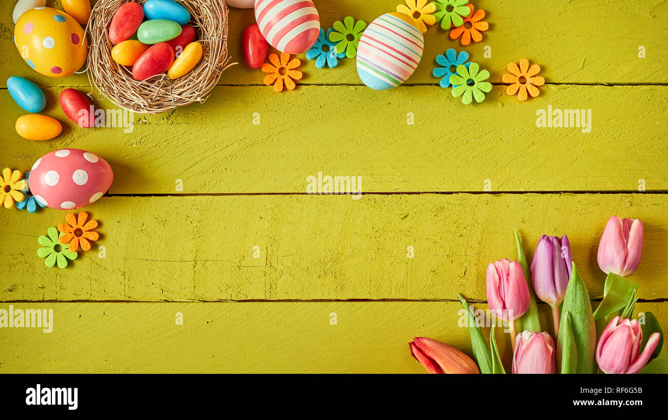 Colorido bodegón con huevos de pascua y primavera fresca flores dispuestas en las esquinas opuestas sobre tablones de madera verde con el centro espacial de copia Foto de stock