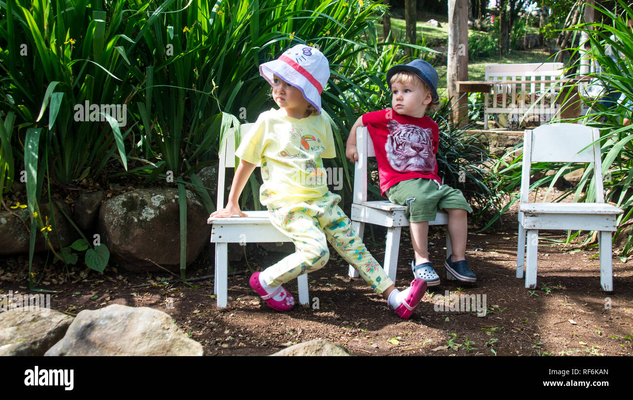 Una foto de un niño y una niña sentados juntos en silla blanca en un jardín. Foto de stock