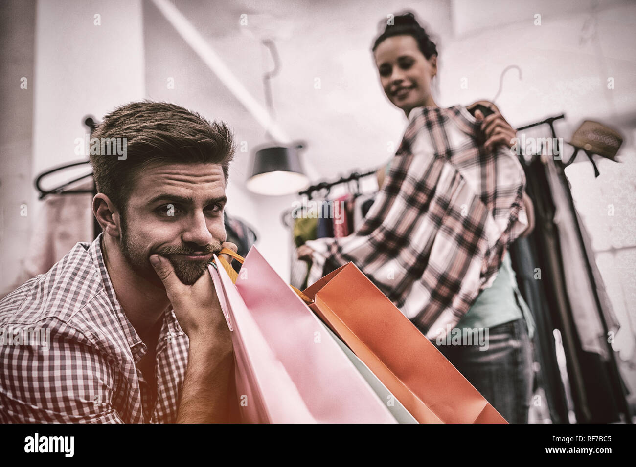 Aburrido hombre con bolsas de compras mientras la mujer por perchero Foto de stock