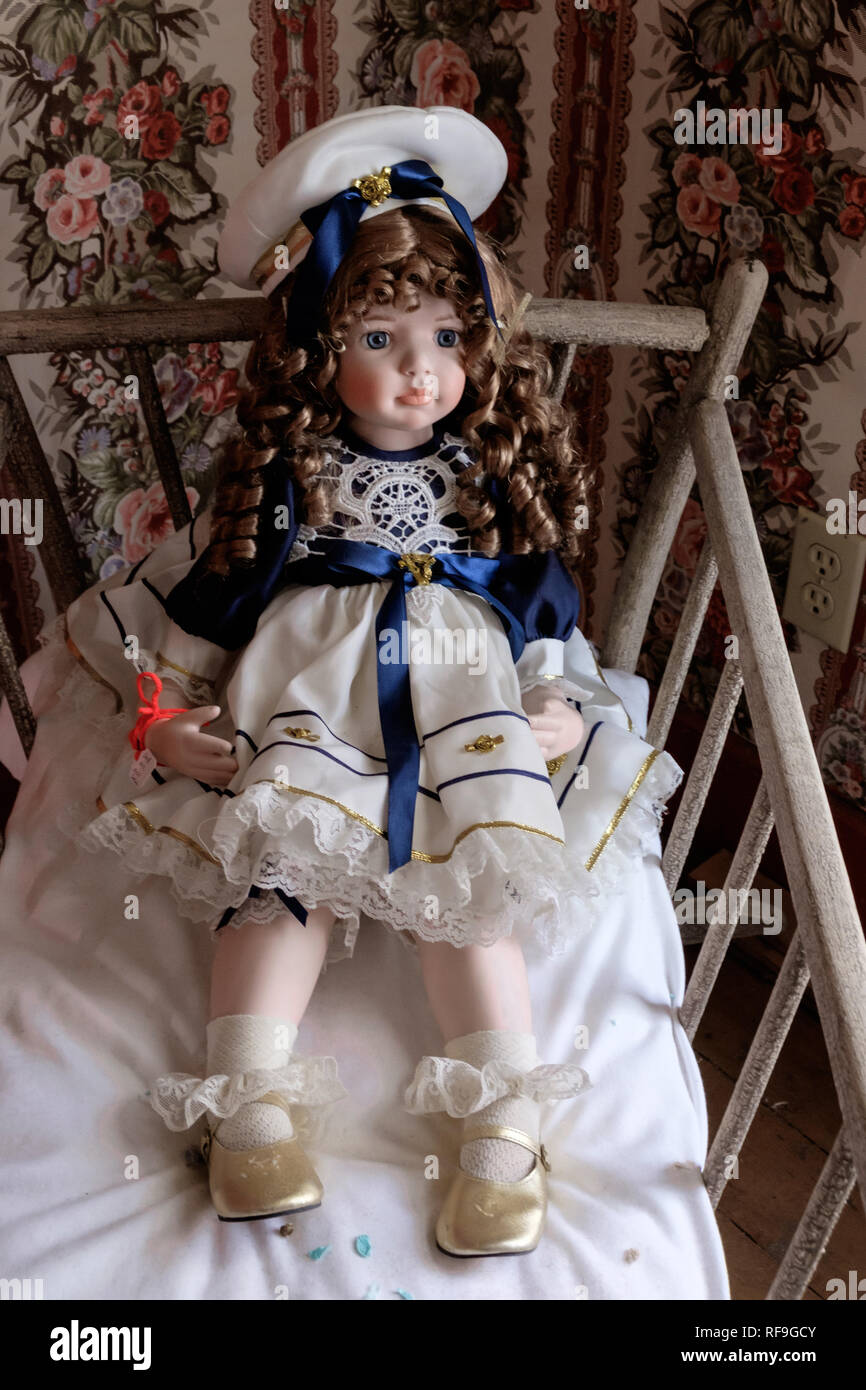 Baby doll Vintage cama con Antique Doll con rizos en Victoriano rojo vestido de marinero y sombrero. Zapatos de satén con volante calcetines, papel de pared vintage victoriana. Foto de stock