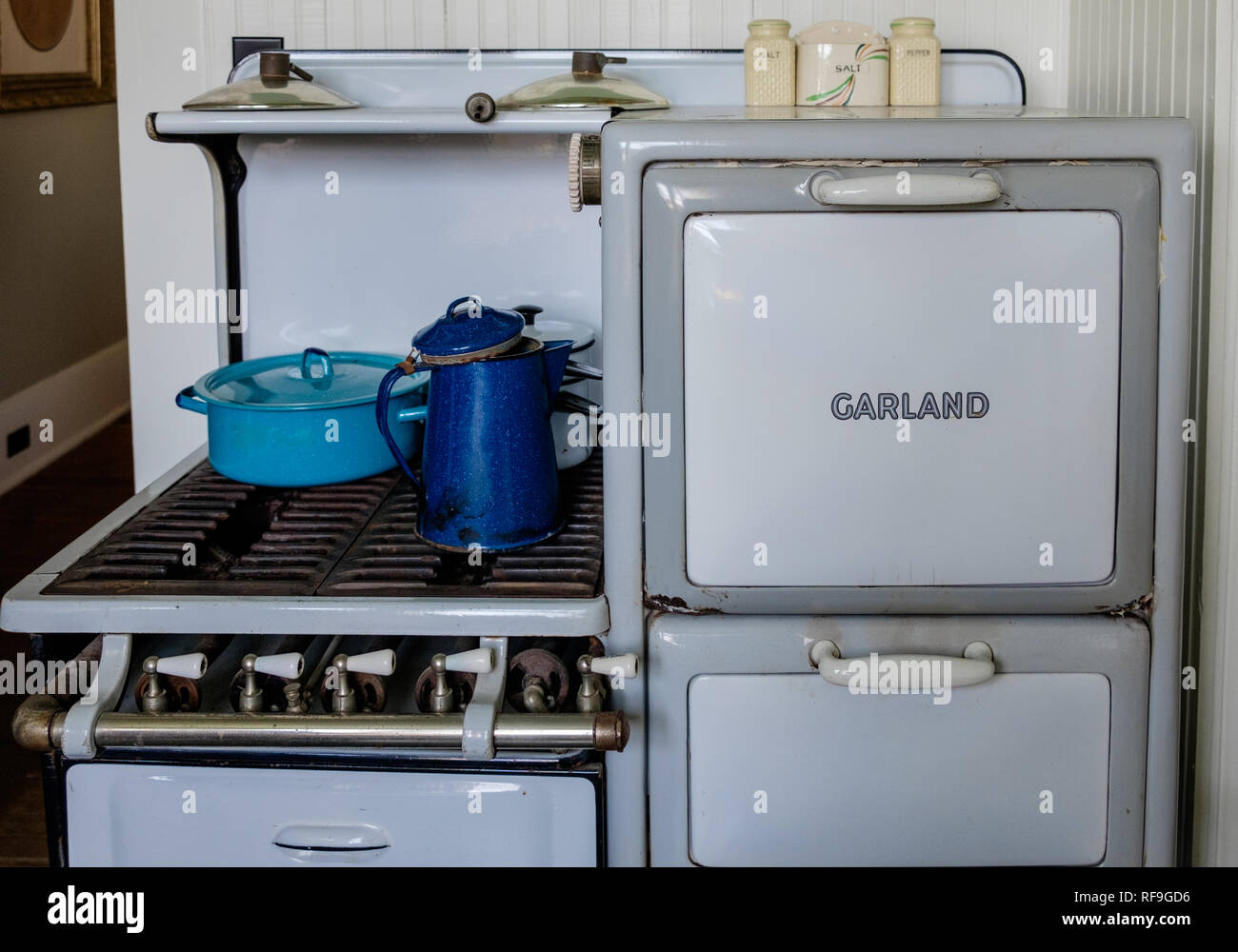 Antique Garland cuatro quemadores de gas estufa de porcelana blanca con puertas y piernas. Dos azul y un esmalte blanco vintage utensilios de cocina. Foto de stock