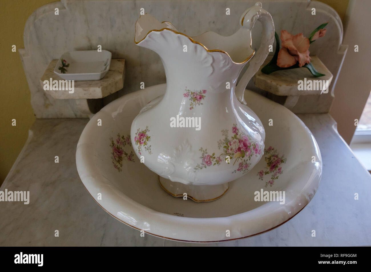 Vintage de cerámica con jarra de agua de la cuenca. Rim festoneado con cantos dorados y rosa diseño floral. Sobre la mesa de mármol. Foto de stock