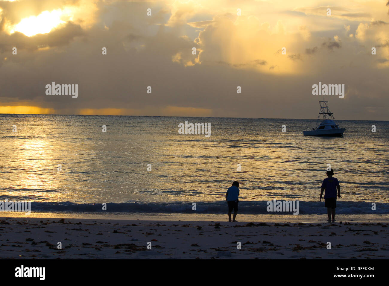 Atardecer tropical en el Caribe, las Islas de Las Bahamas. Puesta de sol  sobre el mar con un barco y dos niños en la playa, en Long Island, Bahamas  Fotografía de stock -