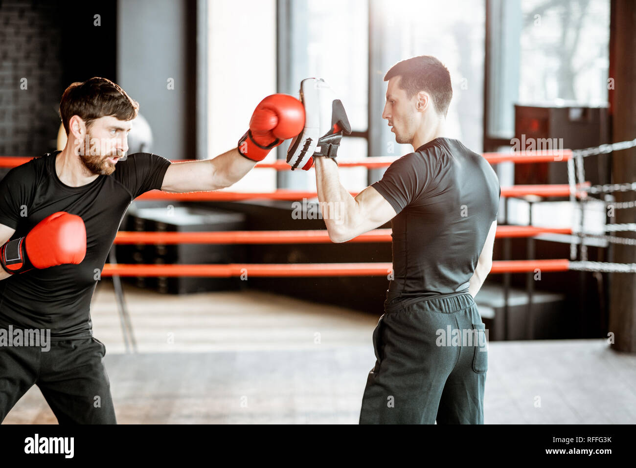 Athletic hombre combates durante la capacitación con instructor de boxeo en el cuadrilátero de boxeo en el gimnasio Foto de stock