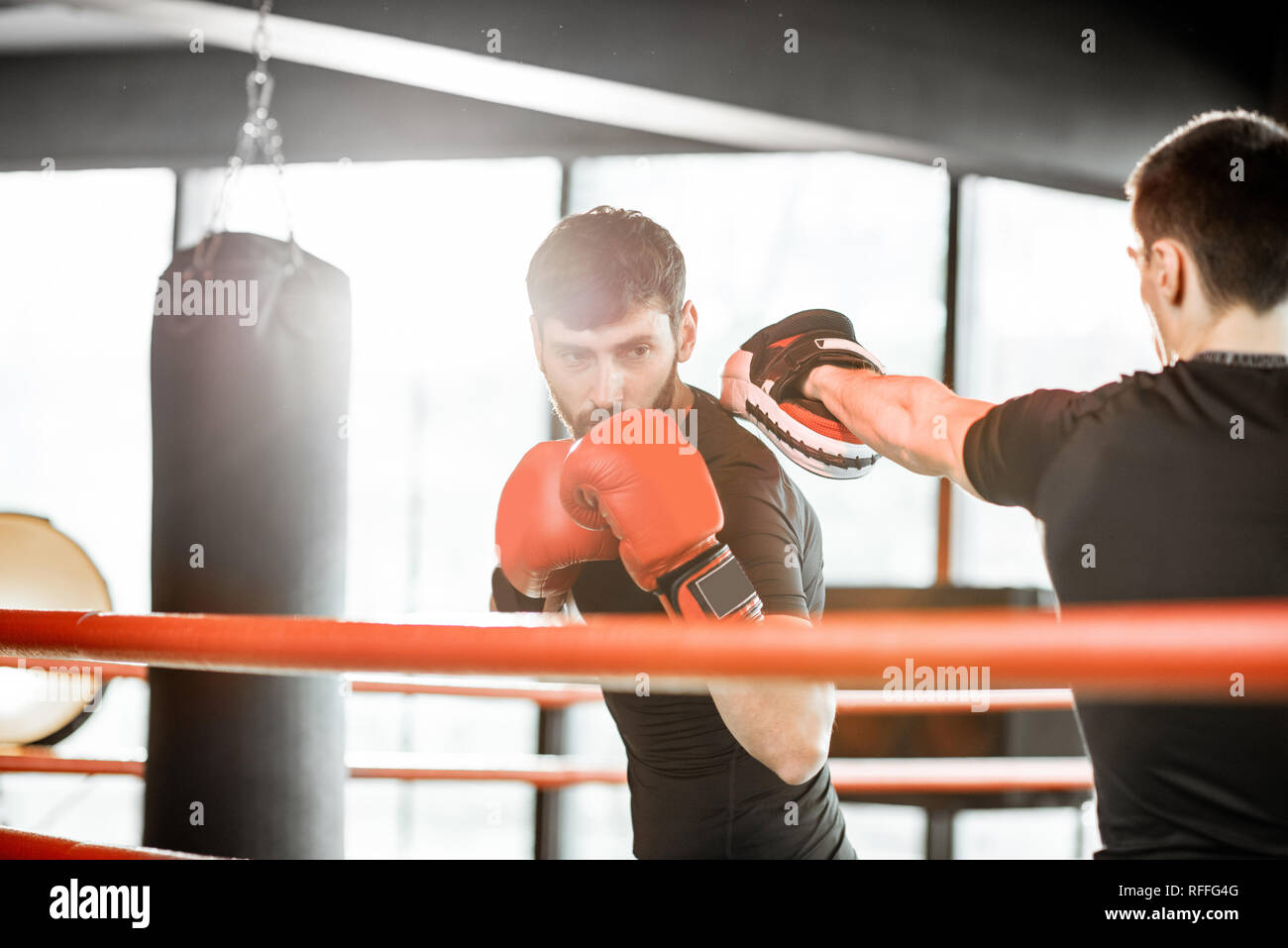 Athletic hombre combates durante la capacitación con instructor de boxeo en el cuadrilátero de boxeo en el gimnasio Foto de stock