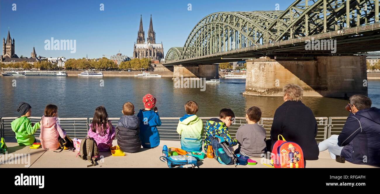 Grupo de niños haciendo un picnic en el rin Boulevard con la catedral de Colonia y el puente Hohenzollern en el fondo Foto de stock