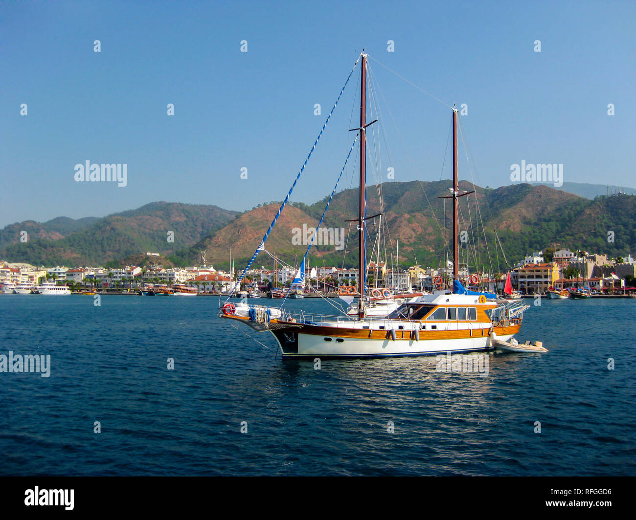 Placer yate fuera del puerto hacia el mar abierto. En el fondo, el puerto de la ciudad balnearia con el telón de fondo de montañas. Foto de stock