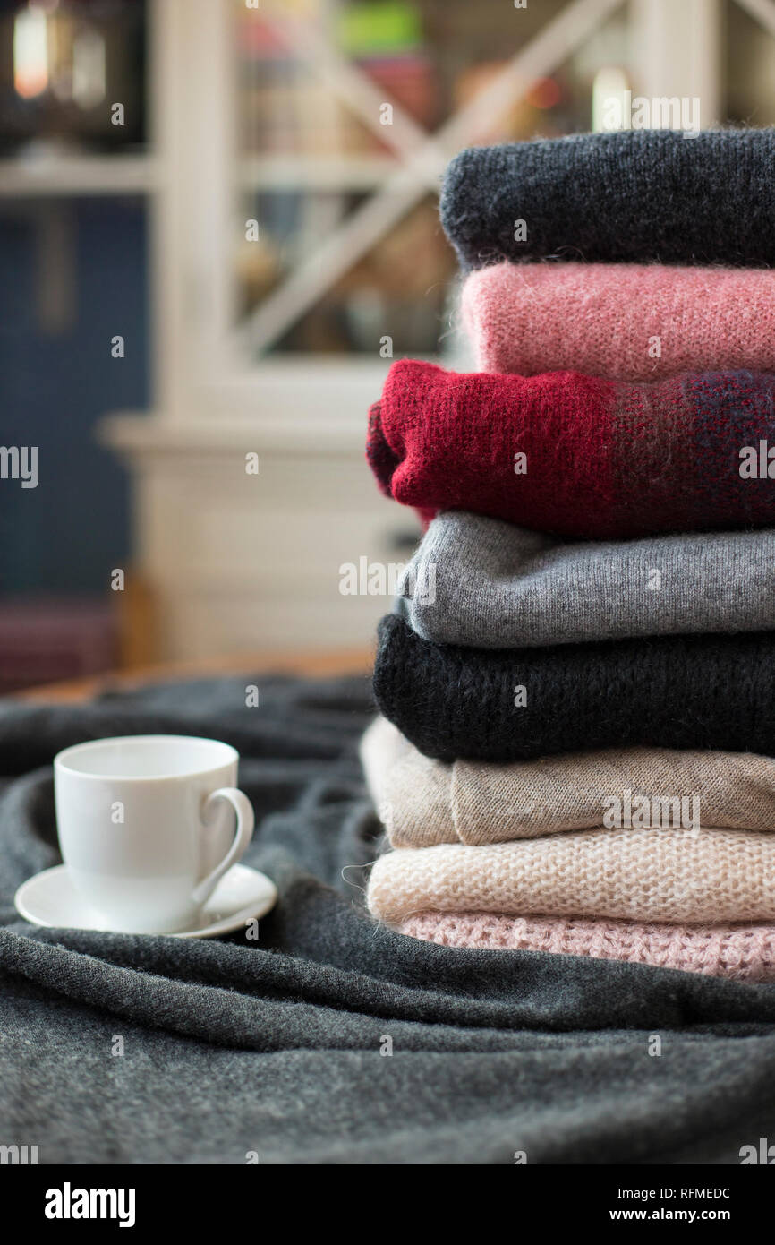 Montón de coloridos suéteres con bebida caliente taza blanca en el lateral, fondo con copia, acogedor espacio hygge papel tapiz. Foto de stock