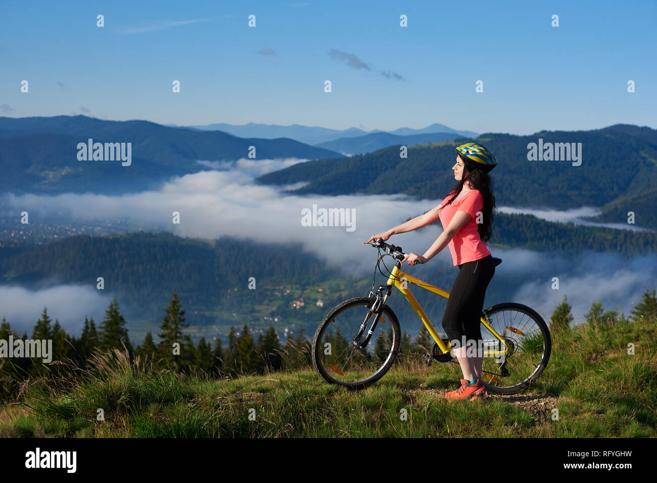 Deportivo ciclista femenino con amarillo en bicicleta en la montaña, con  casco y rojo camiseta roja en la mañana. Montañas, bosques de niebla  borrosa en la b Fotografía de stock - Alamy