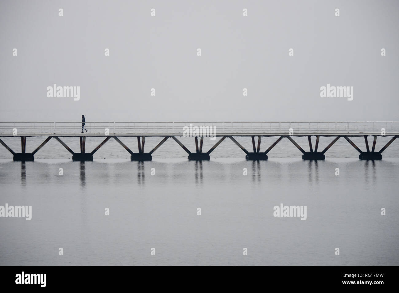 Hombre solitario caminando sobre un puente sobre el agua en Lisboa, ambiente neblinoso, copyspace Foto de stock