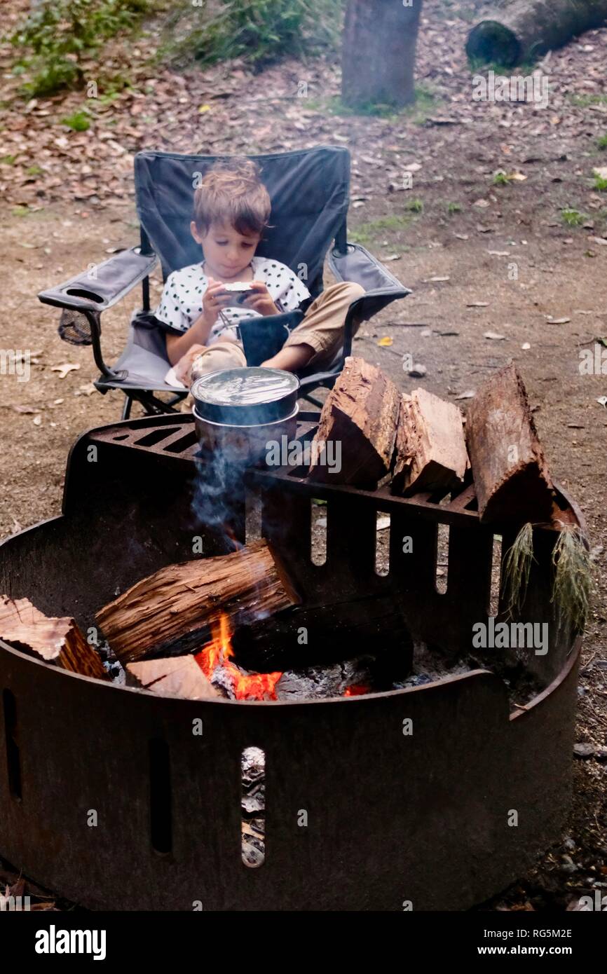 Una chica joven sentada cerca de una fogata, helecho camping zona plana, Parque Nacional Eungella, Queensland, Australia Foto de stock