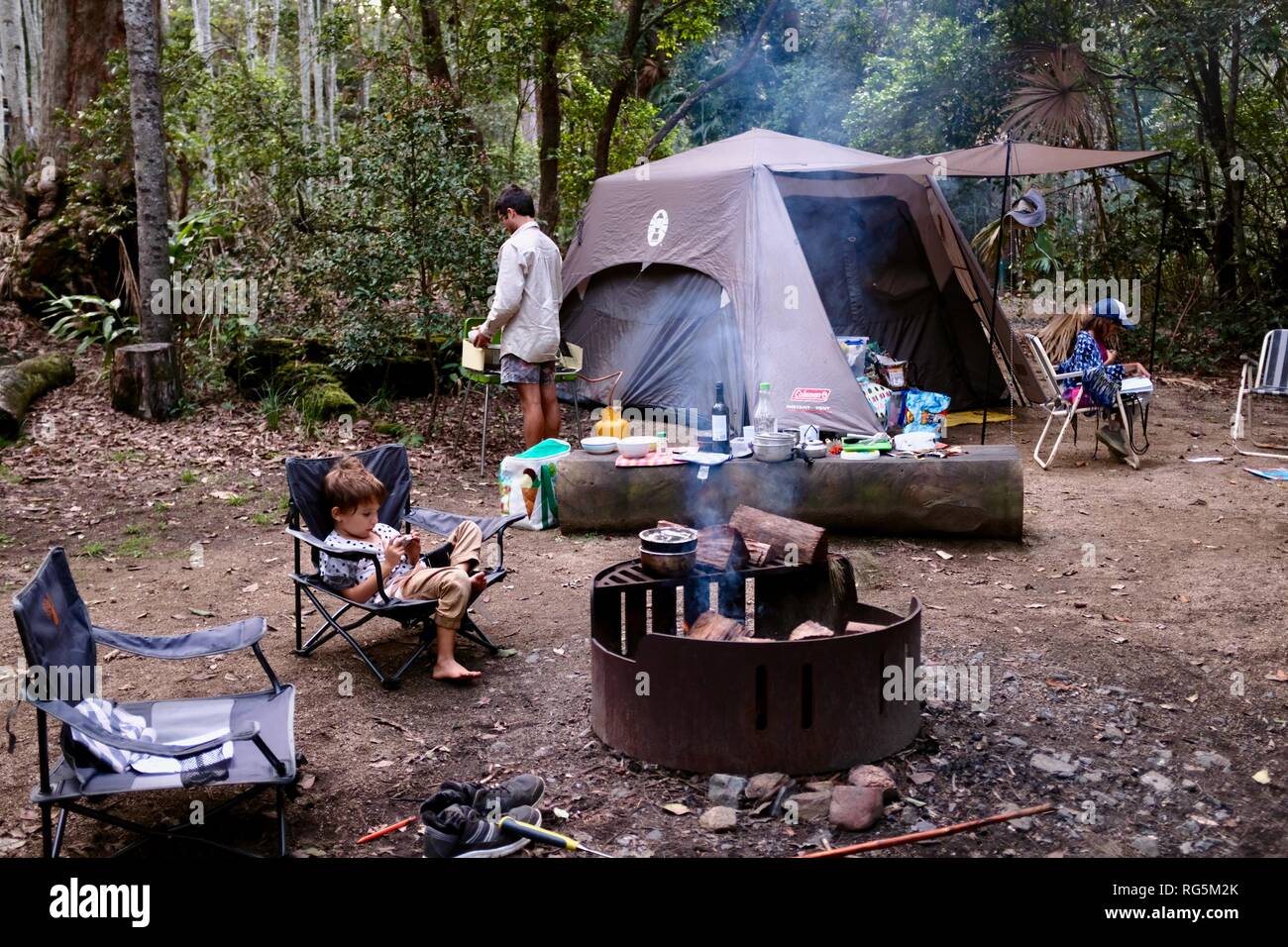 Una chica joven sentada cerca de una fogata, helecho camping zona plana, Parque Nacional Eungella, Queensland, Australia Foto de stock
