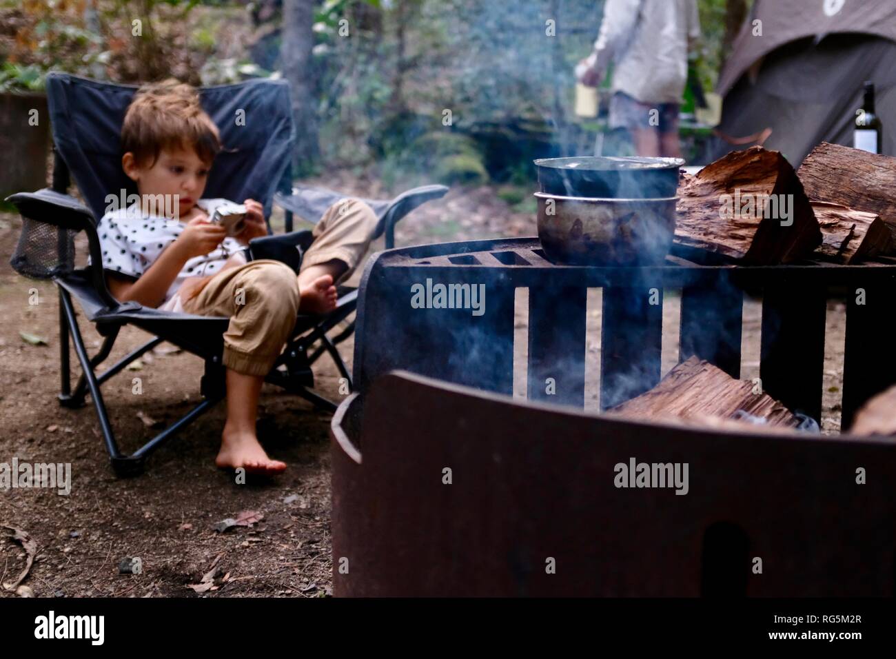 Una chica joven sentada cerca de una fogata, helecho camping zona plana, Parque Nacional Eungella, Queensland, Australia Foto de stock