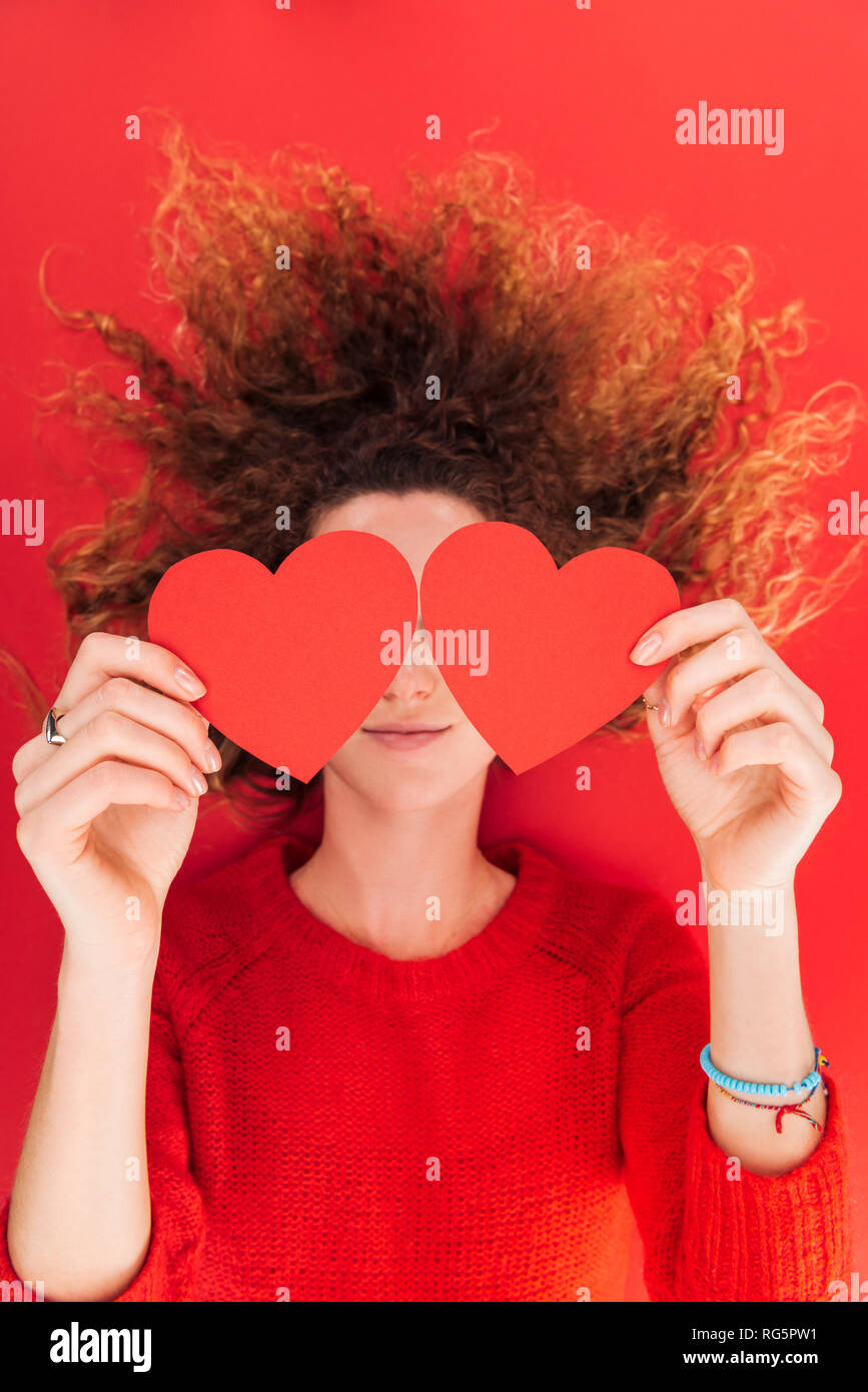 Vista superior de Chica sujetando las tarjetas en forma de corazón en la parte delantera de la cara aislado en rojo, San San Valentín concepto Foto de stock