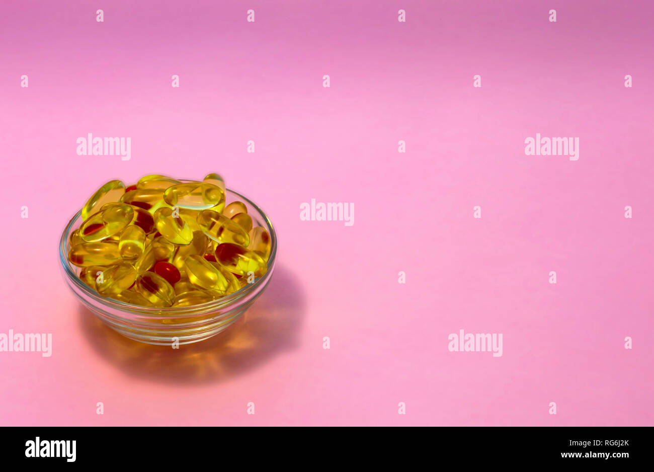 Amarillo transparente cápsulas con aceite de pescado que contienen ácidos Omega-3 en una taza transparente sobre un fondo de color rosa. Foto de stock
