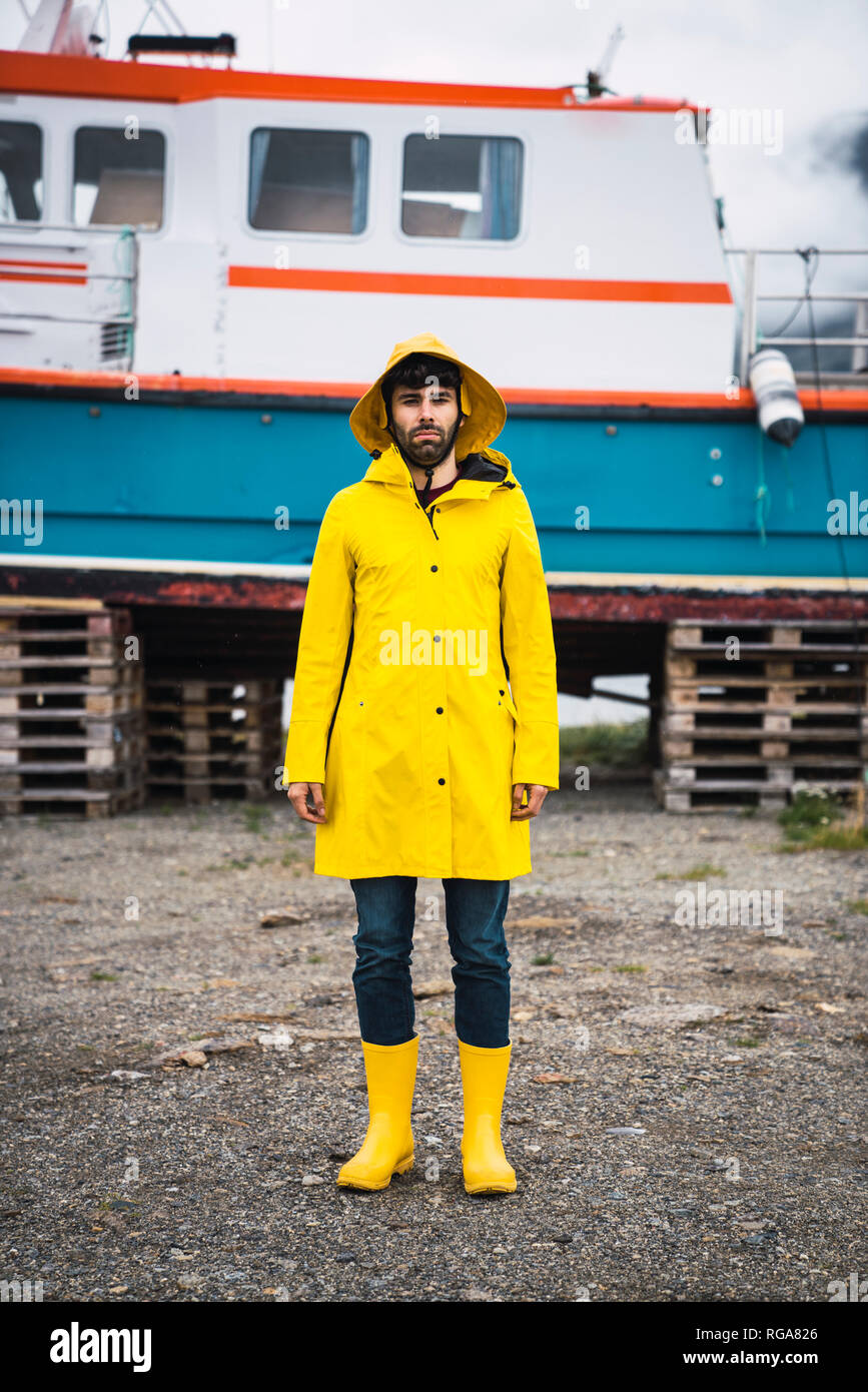 Joven parado en frente de un buque, vistiendo ropa de lluvia, Laponia Noruega Foto de stock