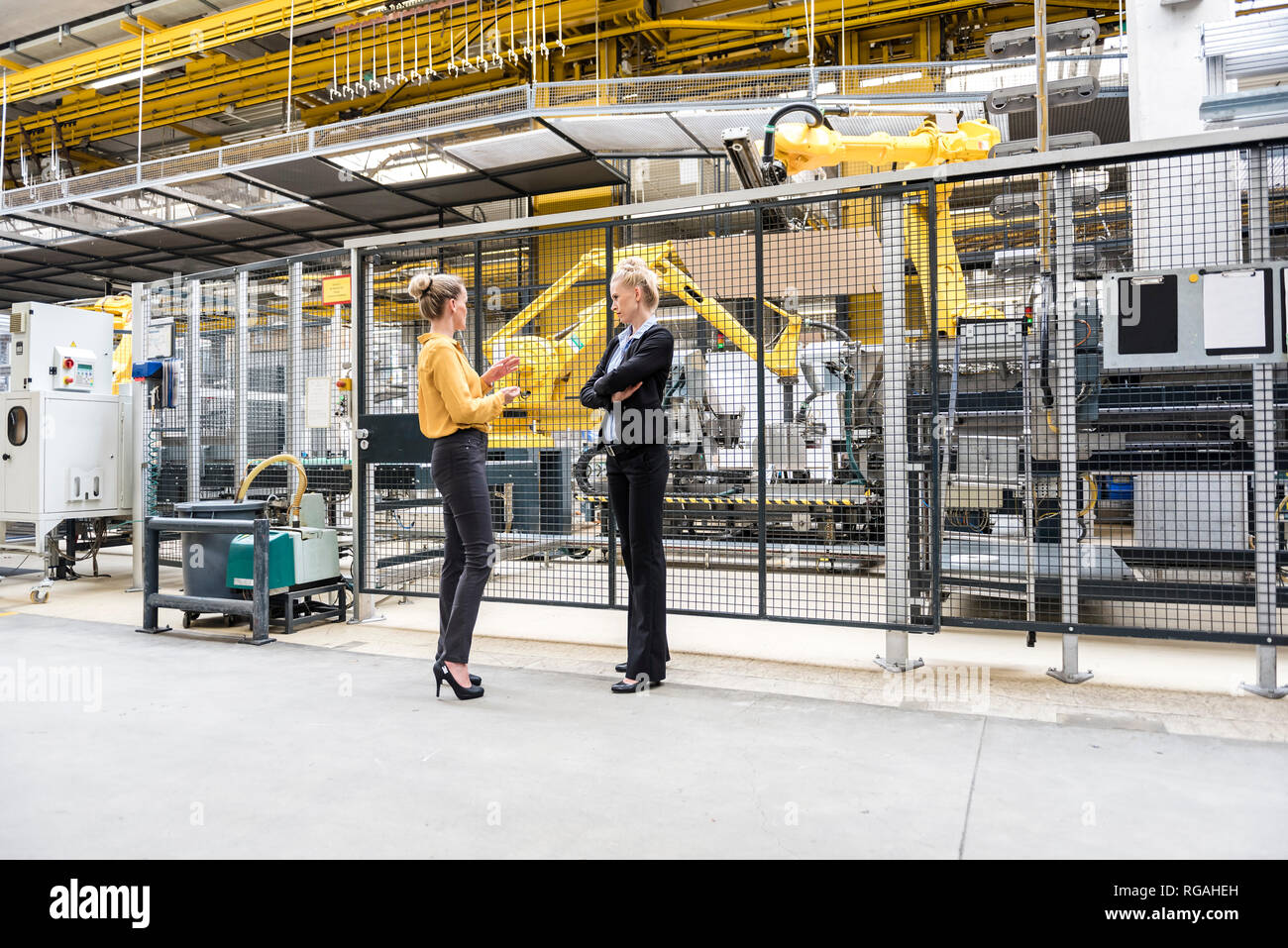 Dos mujeres hablando en la planta de fabricación de fábrica con robot industrial Foto de stock