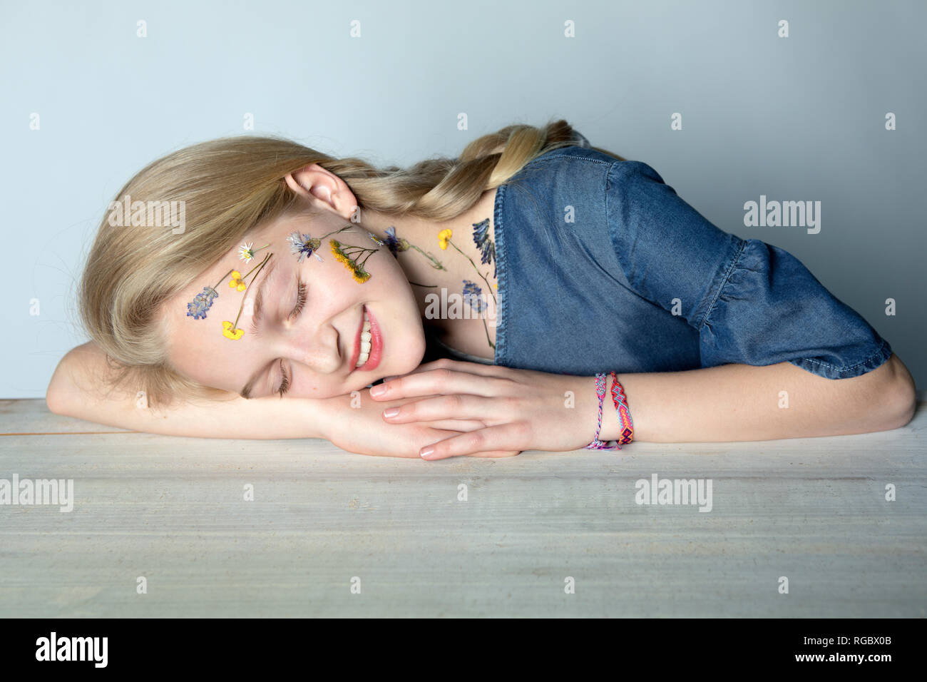 Retrato de sonriente chica rubia con tatuaje de flores presionado en su cara Foto de stock