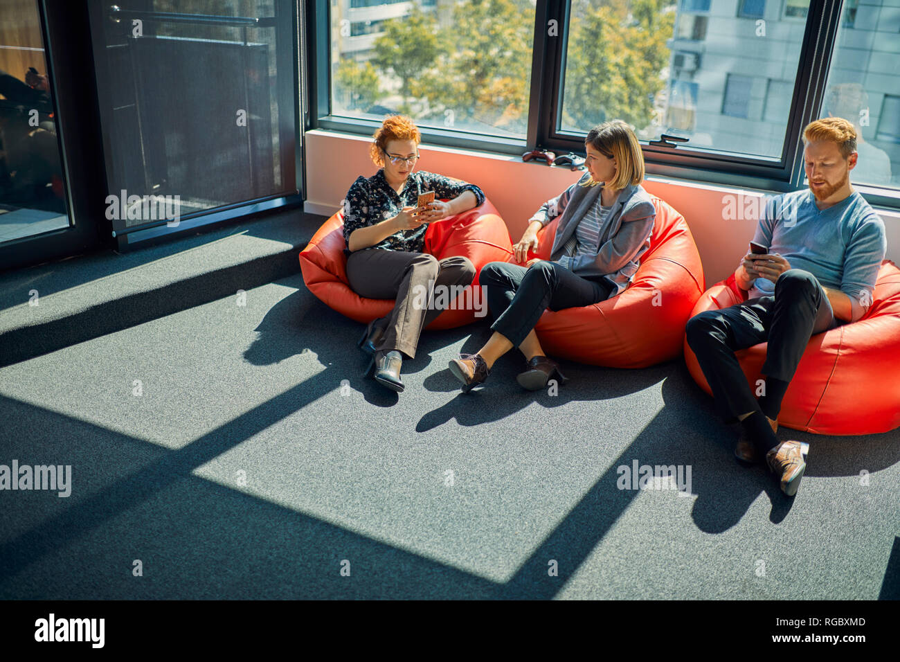 Teléfonos celulares con colegas sentados en sacos de frijoles en Office  lounge Fotografía de stock - Alamy