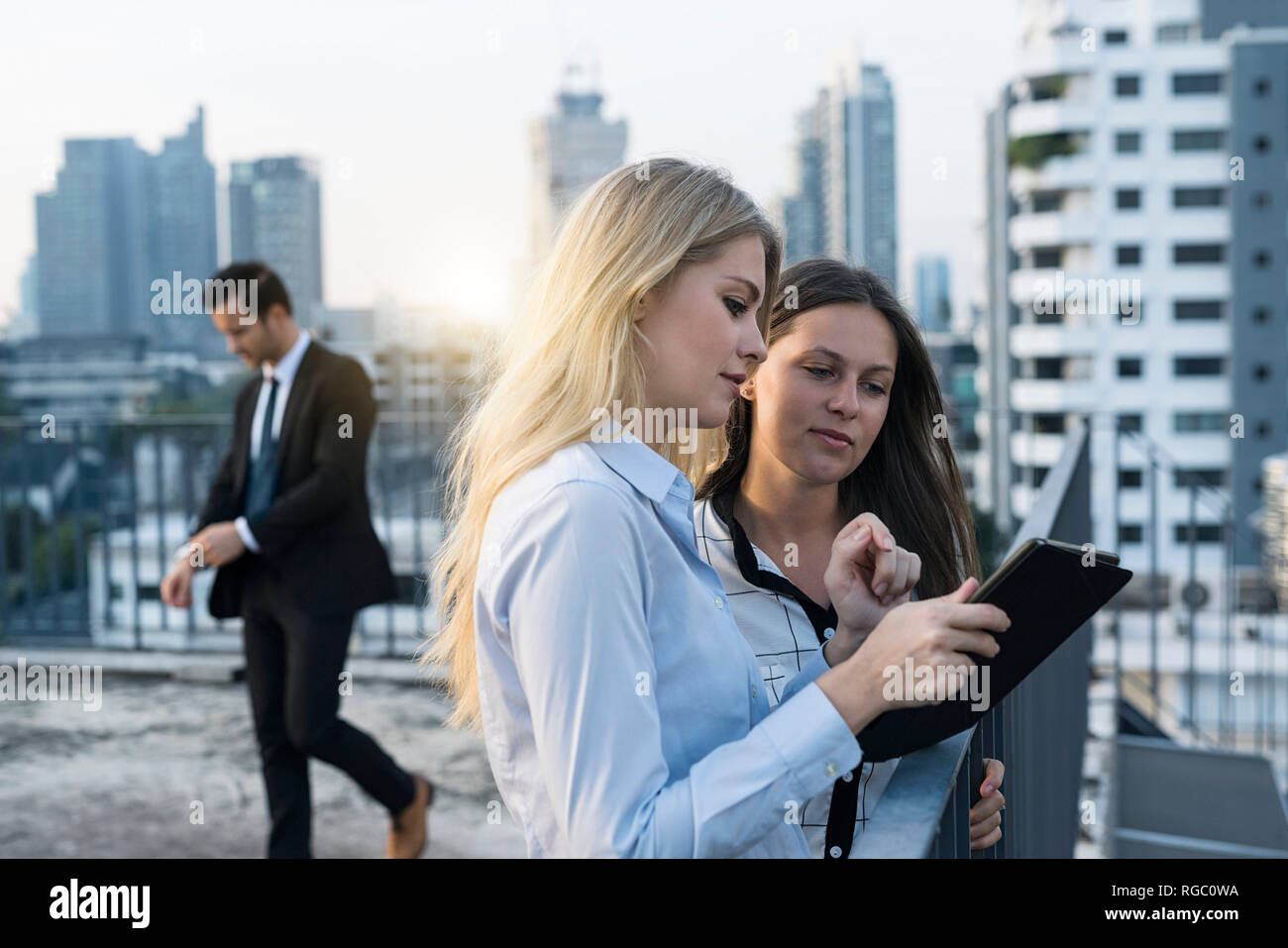 Dos mujeres empresarias hablando en la azotea de la ciudad, utilizando tablet digital Foto de stock