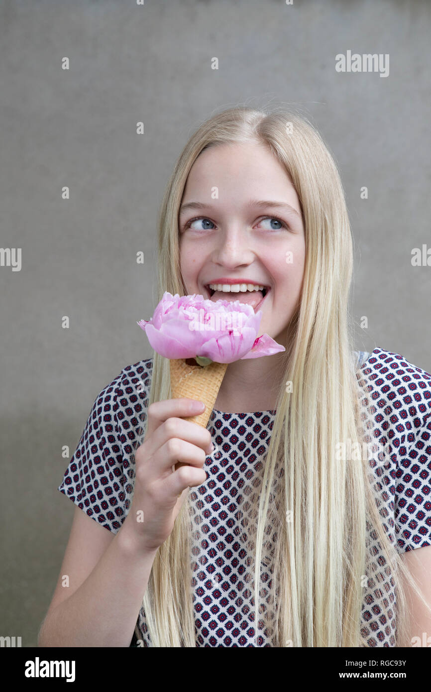 Retrato de chica rubia probando cabeza floral de rosa peonía en cono de helado Foto de stock