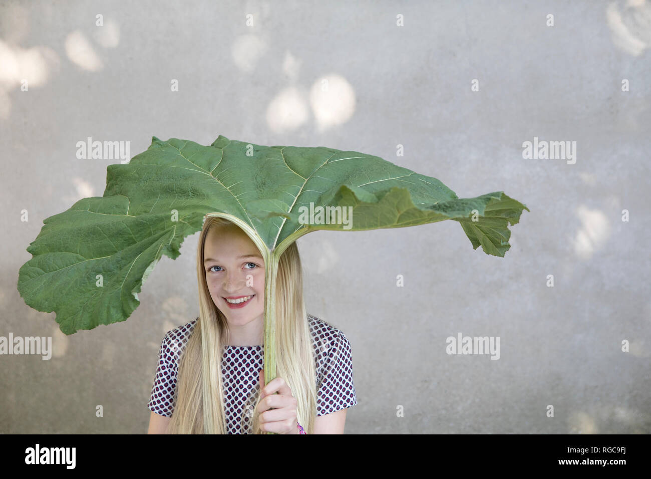 Retrato de chica rubia sonriente bajo grandes hojas Foto de stock