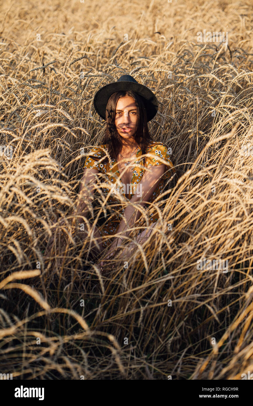 Retrato de joven mujer vistiendo sombrero sentado en el campo de maíz Foto de stock
