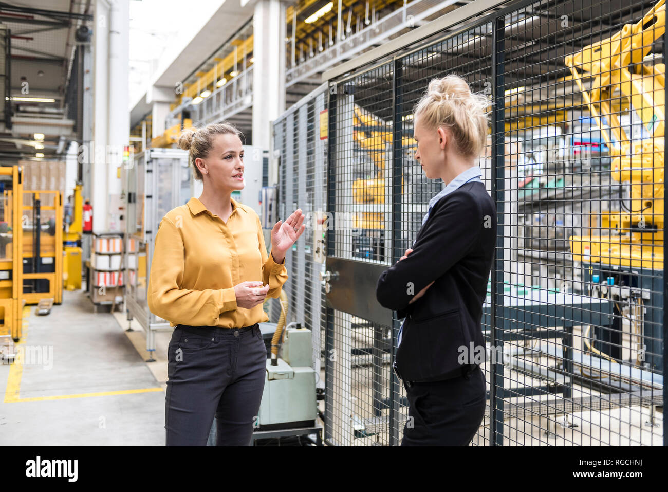 Dos mujeres hablando en la planta de fabricación de fábrica con robot industrial Foto de stock