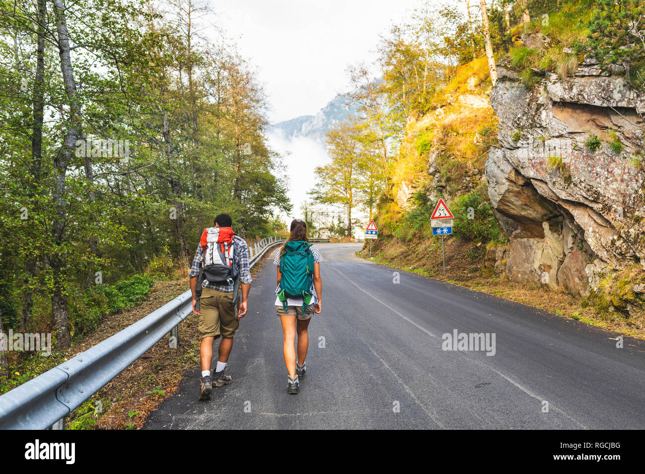 Italia, Massa, vista trasera de la joven pareja caminando sobre el asfalto de los Alpes Apuanos montañas Foto de stock