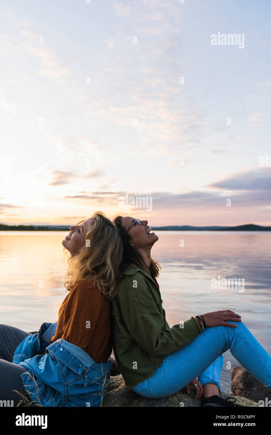 Finlandia, Laponia, dos mujeres jóvenes felices sentados espalda con espalda  en la orilla del lago al atardecer Fotografía de stock - Alamy