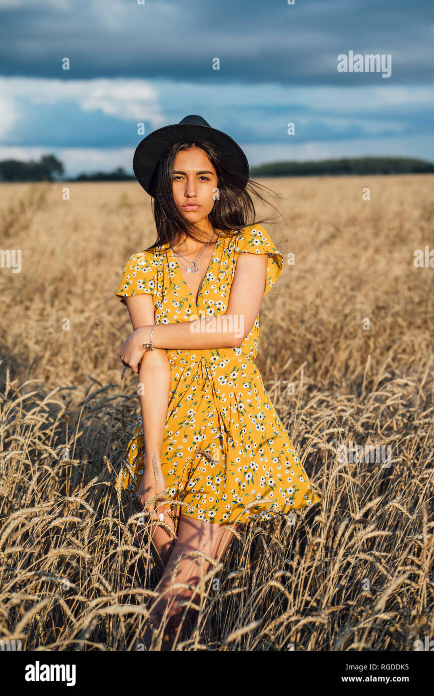 Retrato de joven mujer vistiendo ropa de verano con diseño floral y un sombrero bailando en el campo de maíz Foto de stock