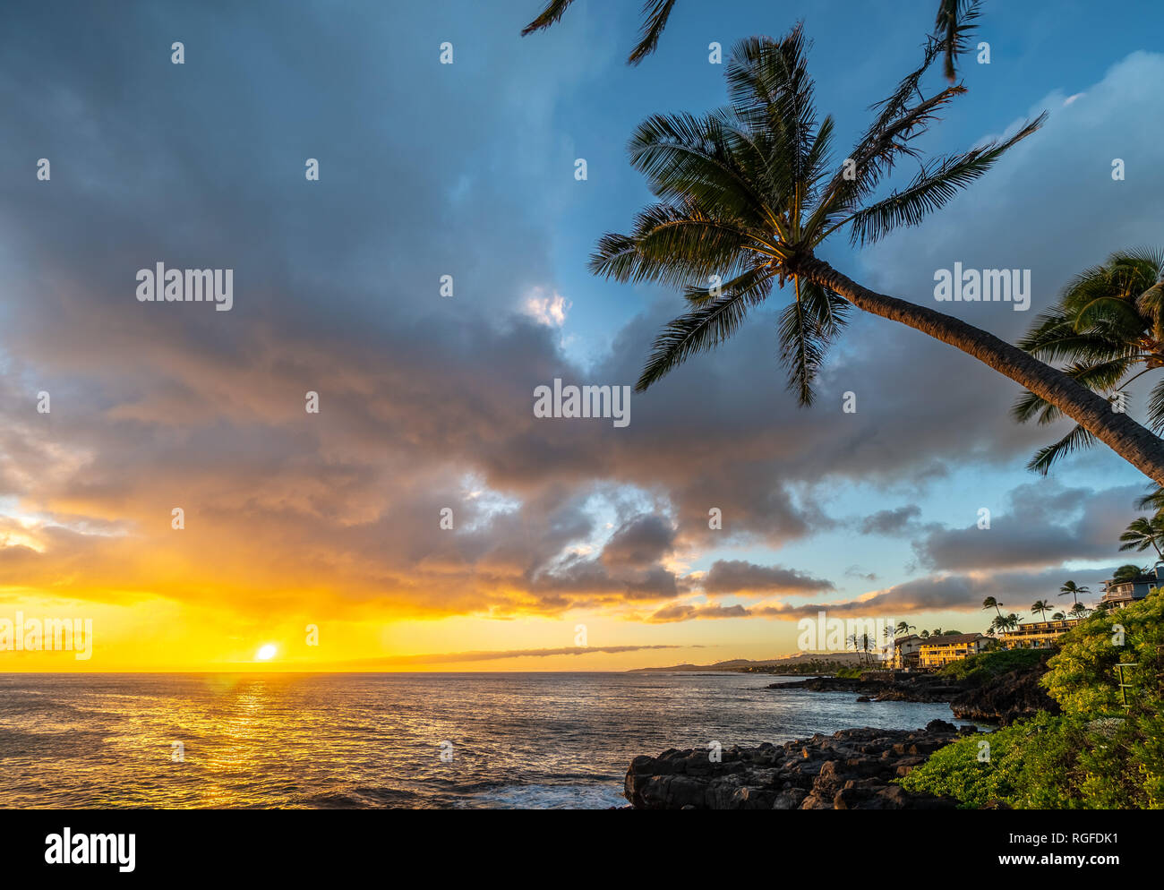 Naranja brillante puesta de sol sobre el océano, con cocoteros a lo largo de la costa rocosa, Poipu, Kauai, Hawai, Koloa Foto de stock