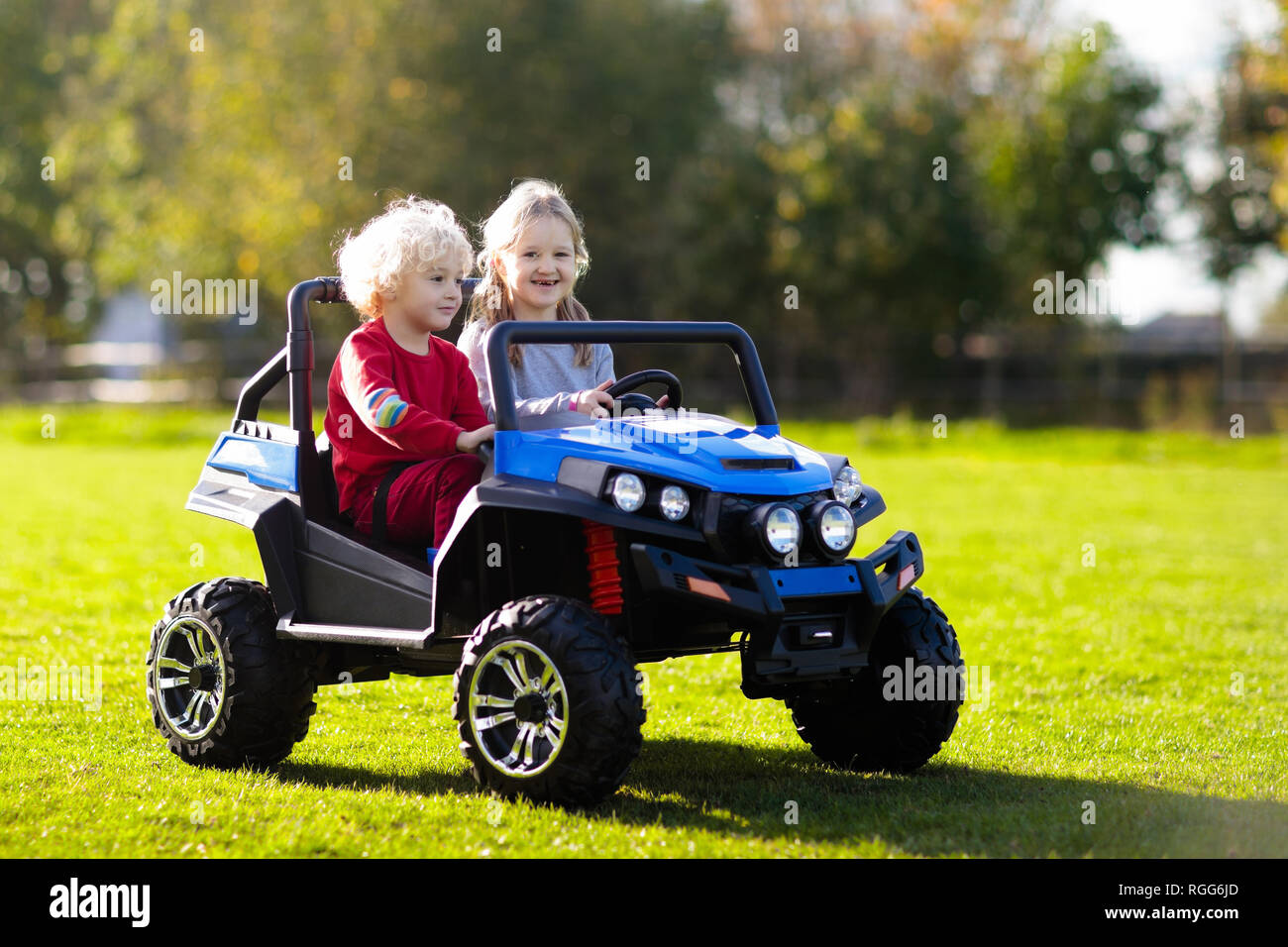 Coche de juguete eléctrico de conducción para niños en verano park. Juguetes  de exterior. Los niños en la energía de la batería vehículo. Chico y chica  camión de juguete en el jardín.