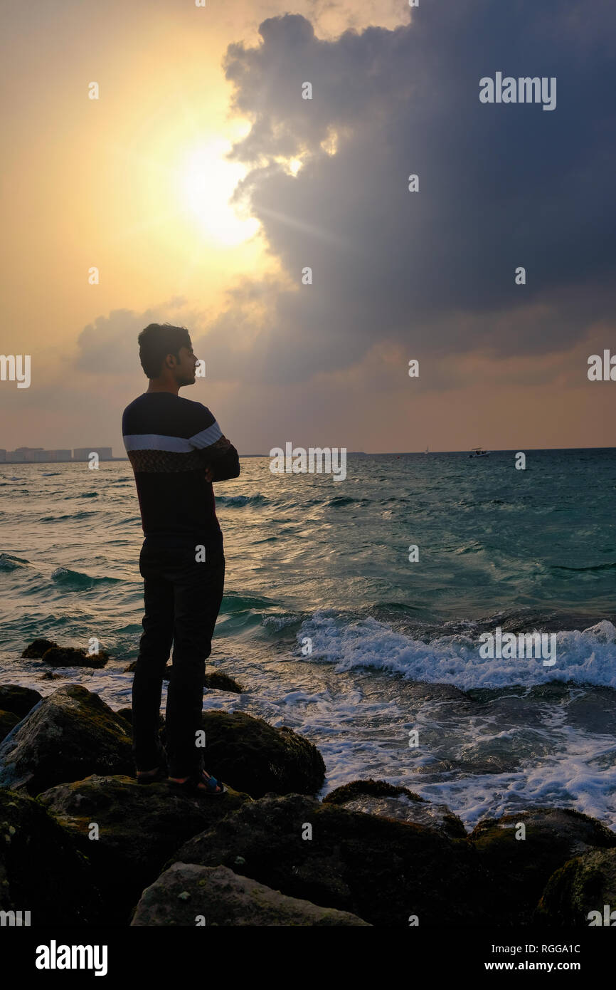 Silueta de un joven adulto de pie sobre las rocas en la playa Foto de stock