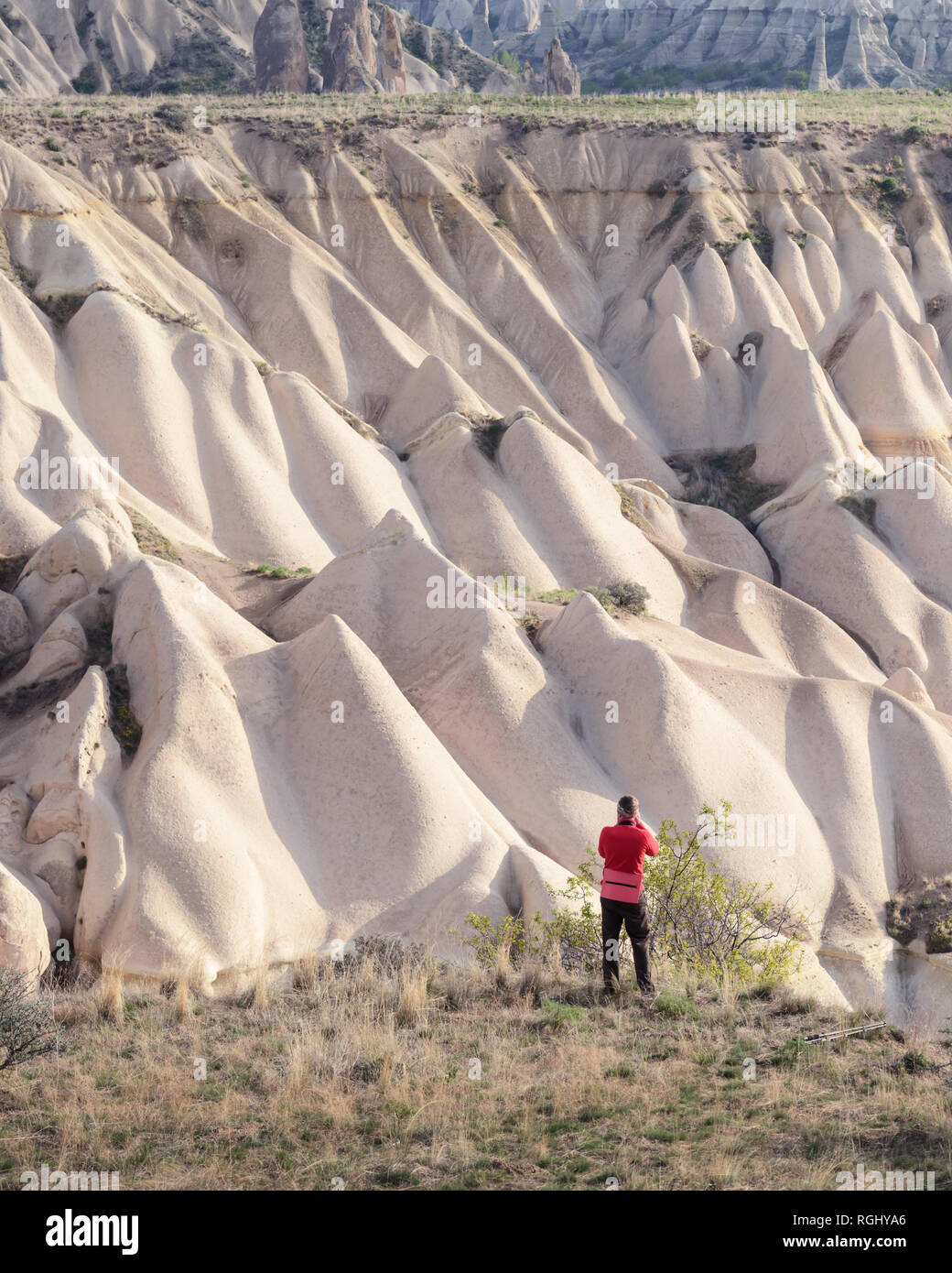 Día increíbles montañas en Cappadocia, Turquía. Fotógrafo en chaqueta roja toma de fotografía increíble de las colinas. Fotografía paisajística Foto de stock