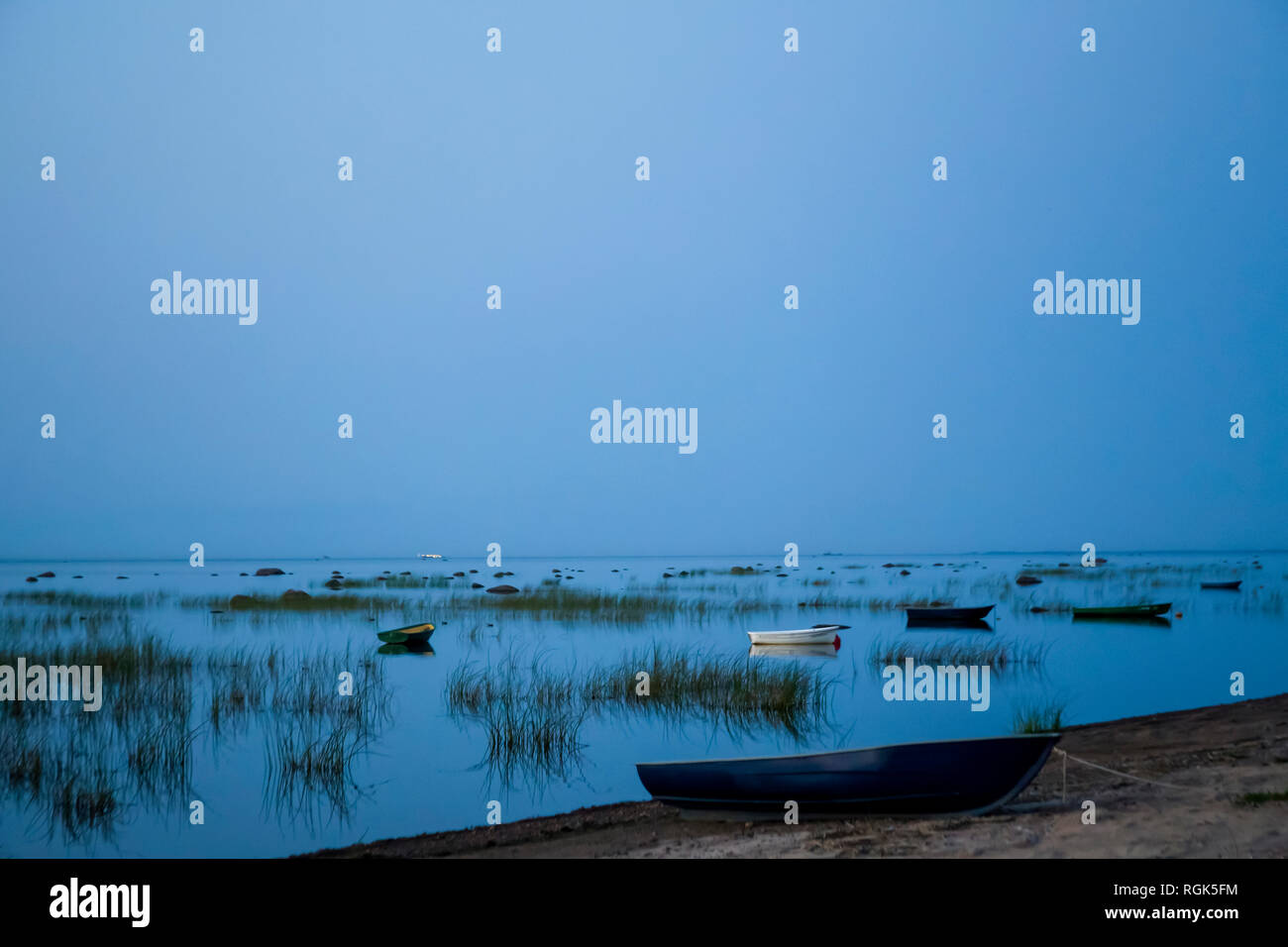 Los botes de pesca anclados en una fila, que se refleja en una clara lago al atardecer. Foto de stock