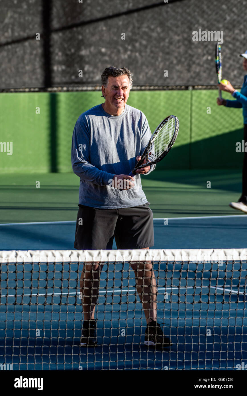 Centrado y ancianos jugador de tenis recreativo listo para la acción mientras dobla partner sirve el balón durante un partido de tenis. Foto de stock
